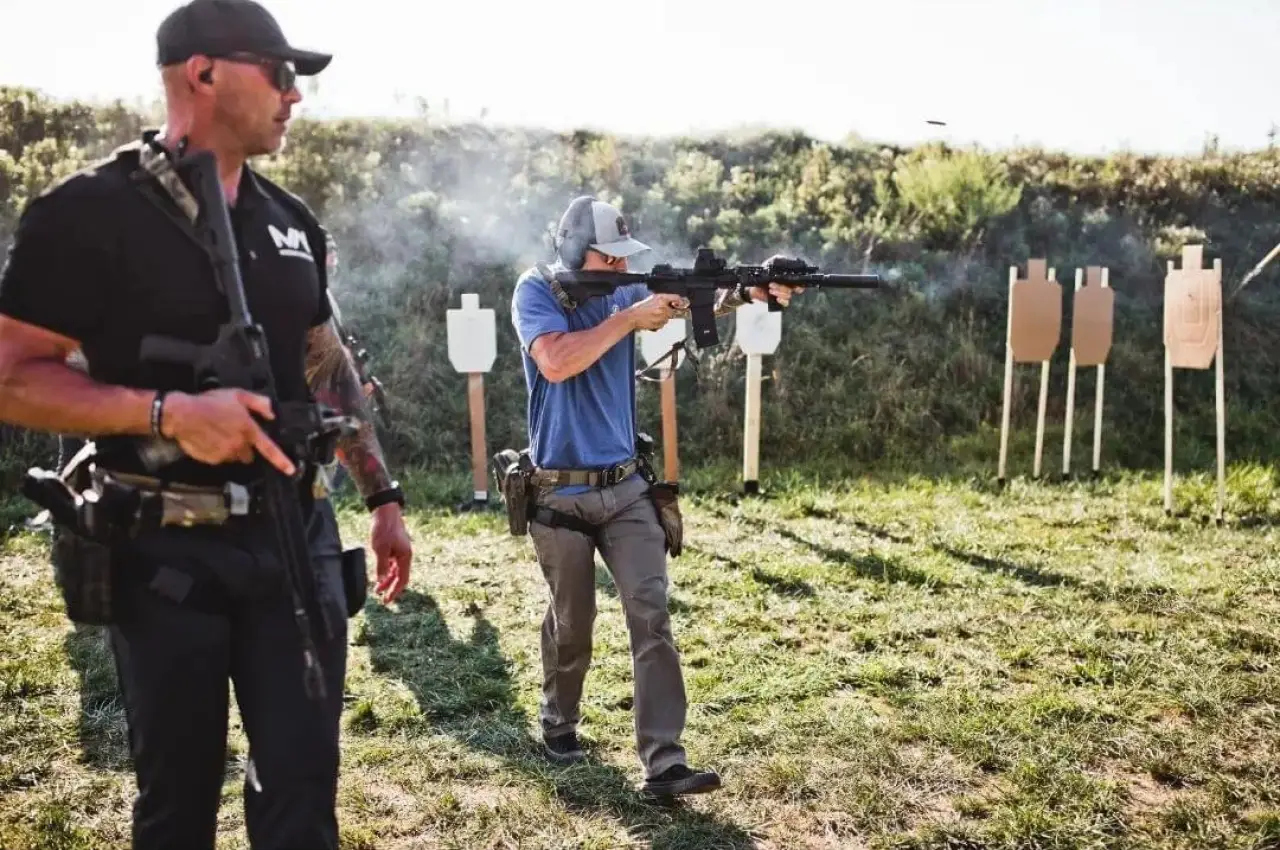 two people practicing shooting at paper targets in an outdoor firing range
