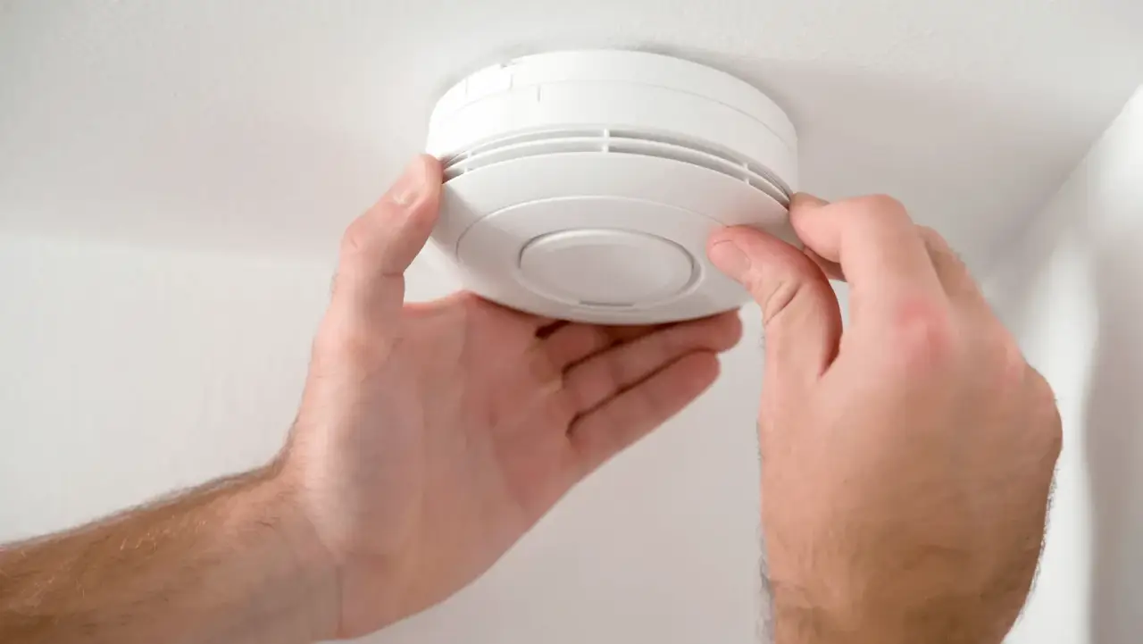 A person installing or testing a smoke detector on a white ceiling.