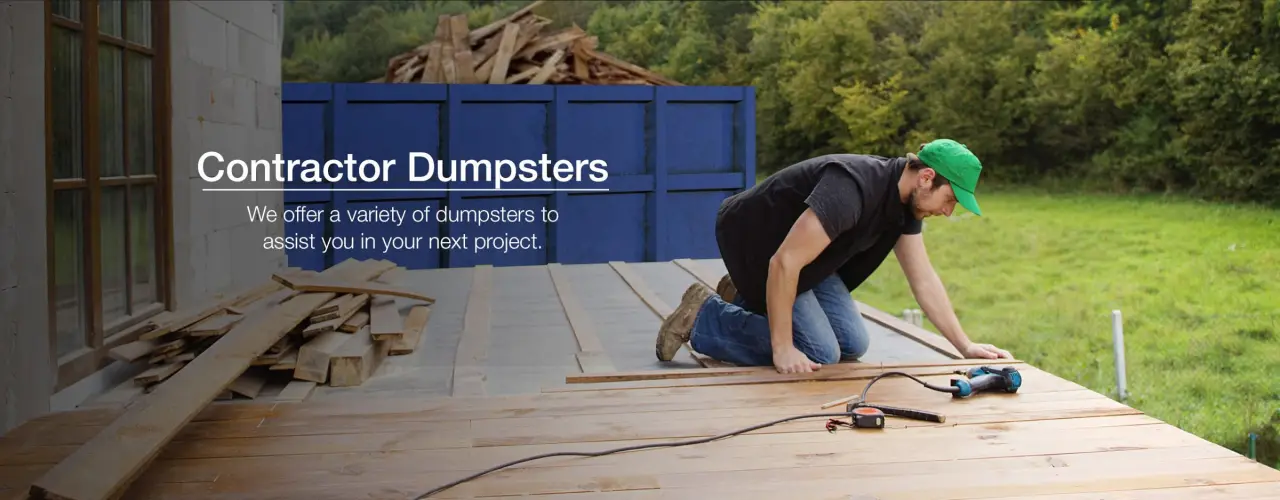 worker putting down new floorboards with old floorboards in dumpster