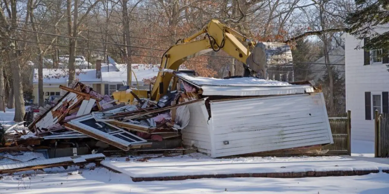 excavator demolishing a white building in the winter