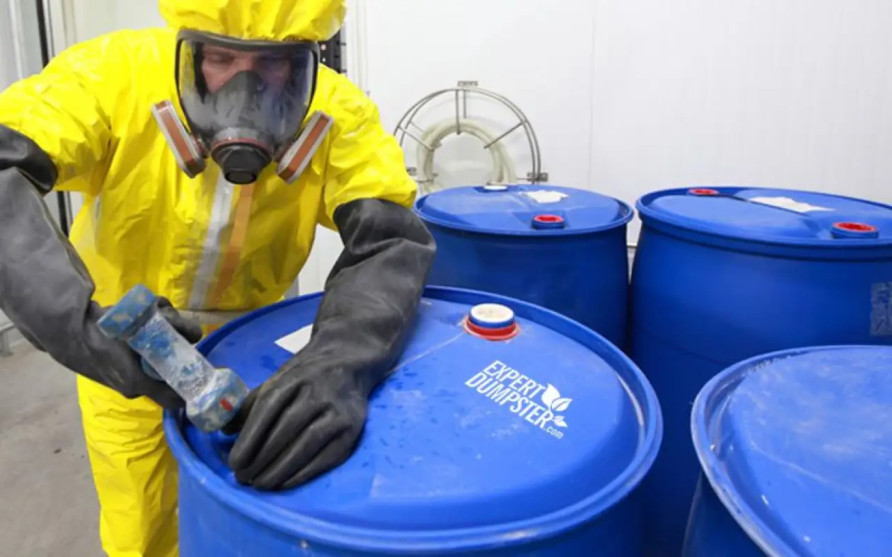 person in hazmat suit handling blue chemical barrels