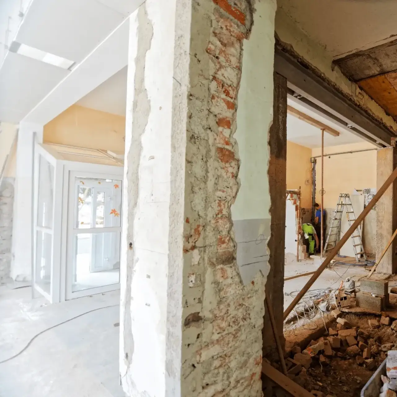 Room under renovation with exposed brick, construction tools, debris, and unfinished walls.