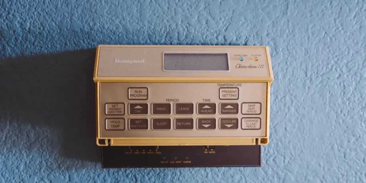 A beige Honeywell thermostat with buttons is mounted on a textured blue wall.