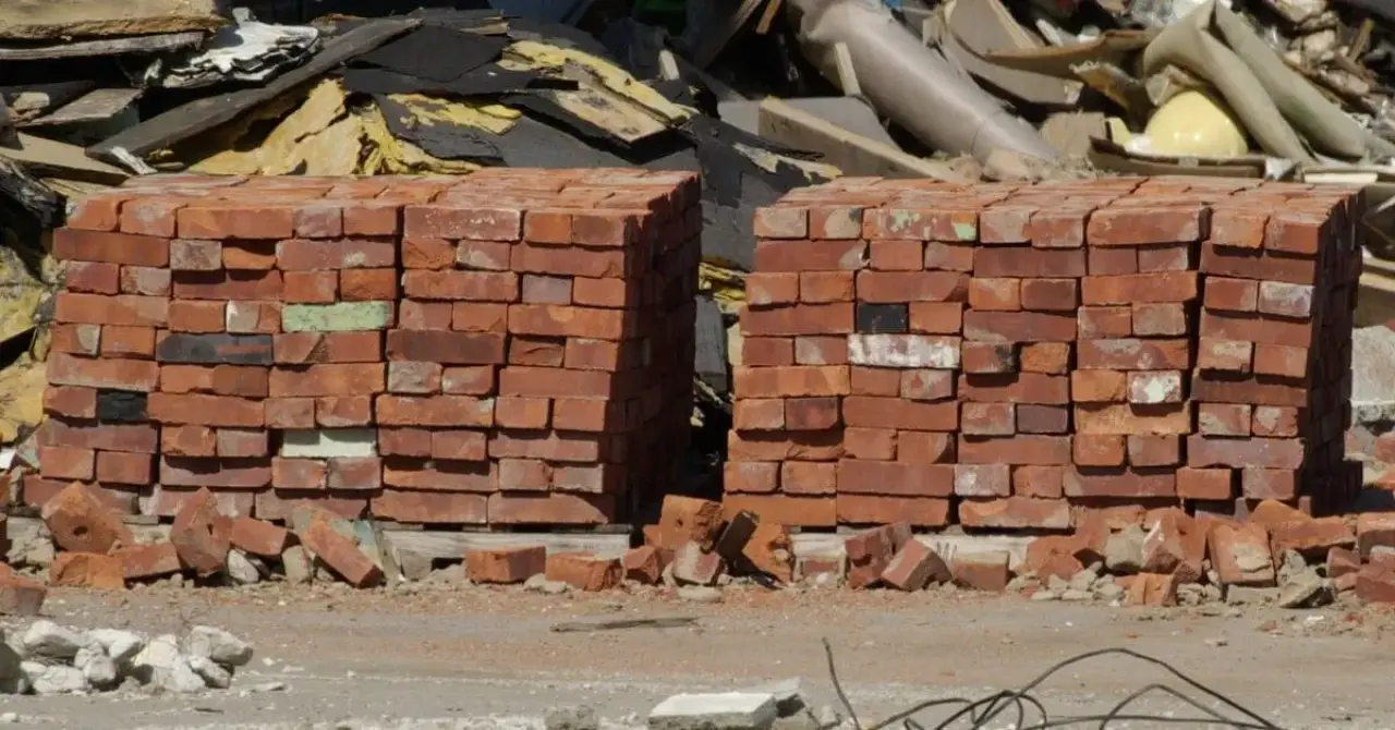 Two stacks of red bricks at a construction site, with debris and rubble scattered around.