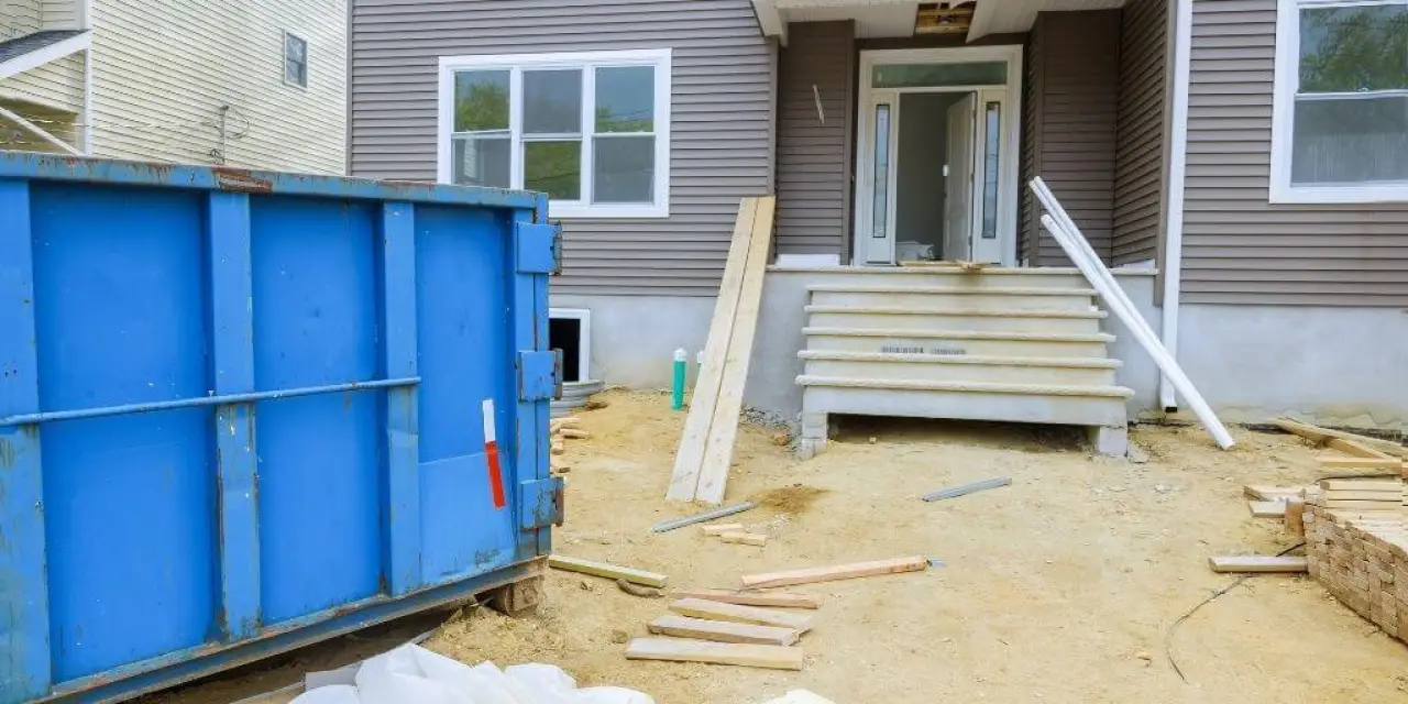 blue dumpster and scattered wood in front of a house under construction