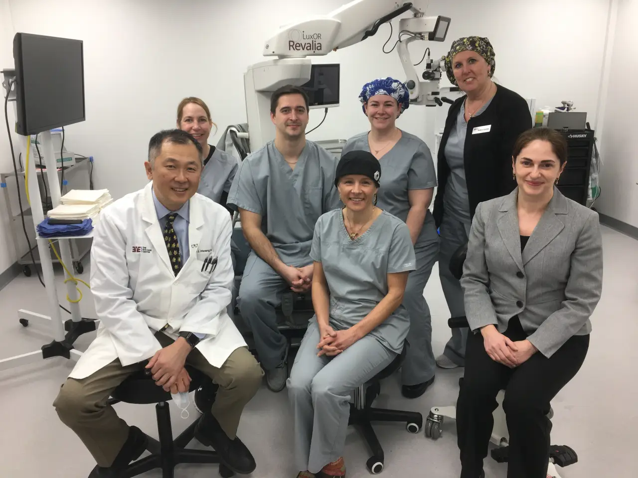 Seven medical professionals pose together in a clinic, with medical equipment in the background.