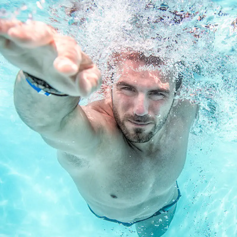 Man swimming underwater, reaching forward with one arm, surrounded by bubbles in a pool.