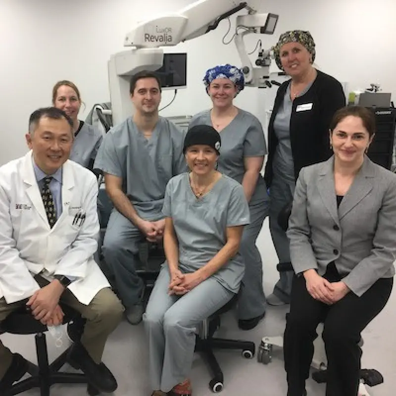 Six medical professionals pose together in a clinic, some in scrubs and others in formal attire.