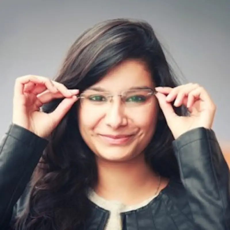 Woman with long dark hair smiles, adjusting her glasses, wearing a black jacket.