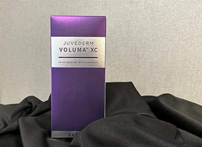 A purple box of Juvéderm Voluma XC injectable gel sits on a black fabric surface.
