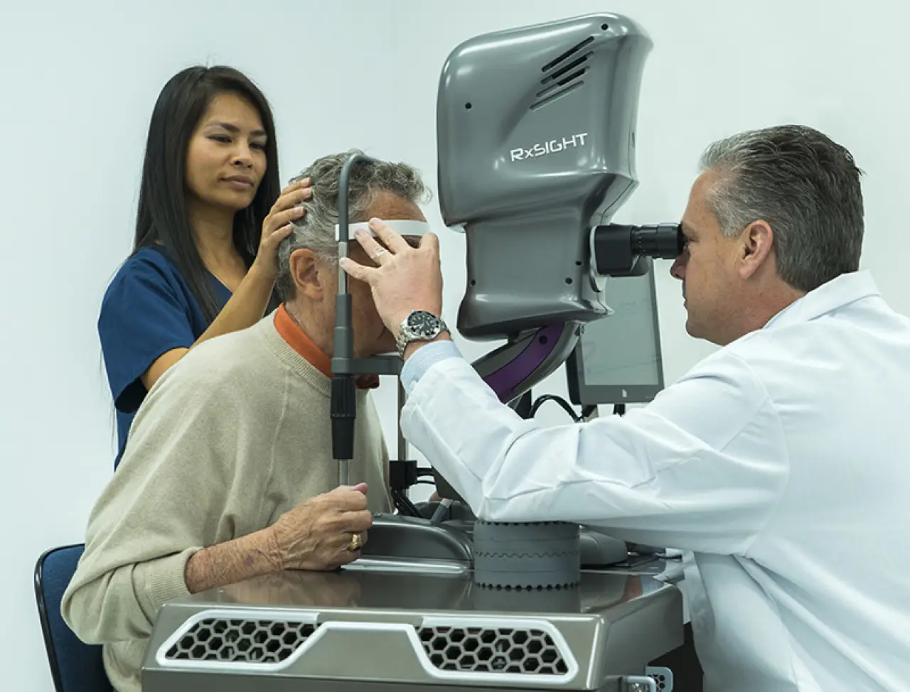 An eye doctor examines an elderly mans eyes with advanced equipment as an assistant helps.