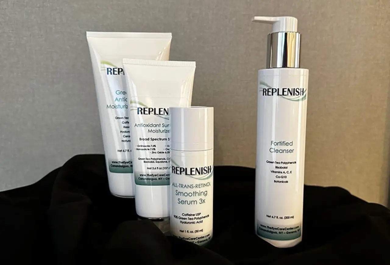 Four REPLENISH skincare products displayed on a black fabric background.
