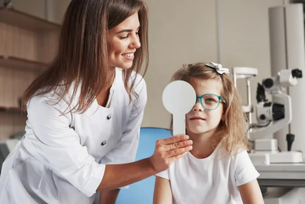 An eye doctor covering a child's right eye during a routine eye exam.