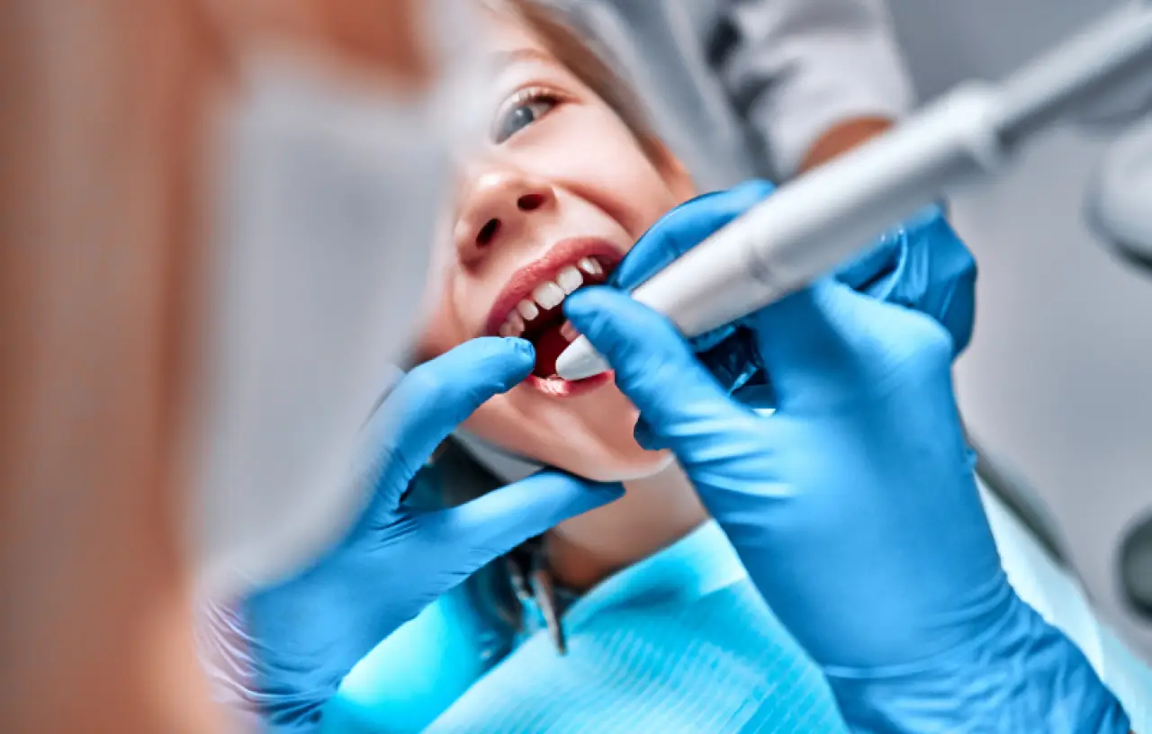 A dentist in blue gloves examines a young childs teeth with dental tools.