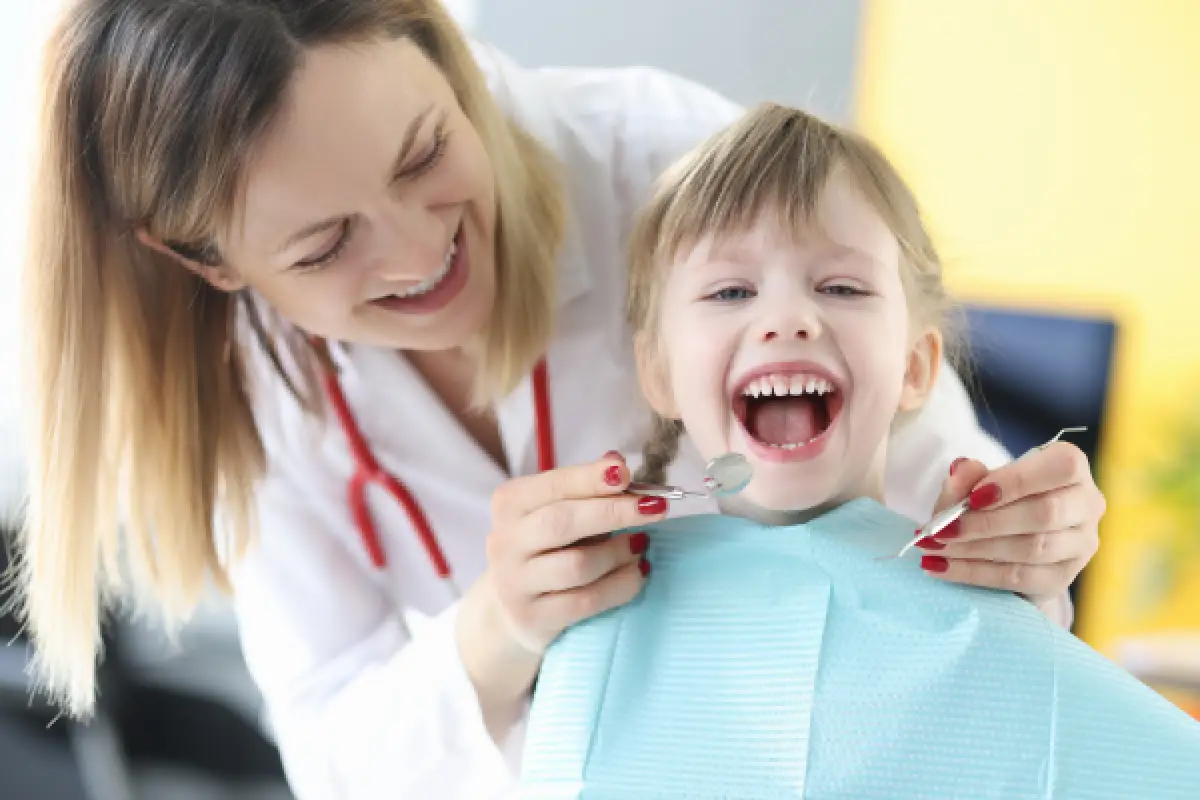 Smiling dentist examines happy young girl’s teeth during a dental checkup.