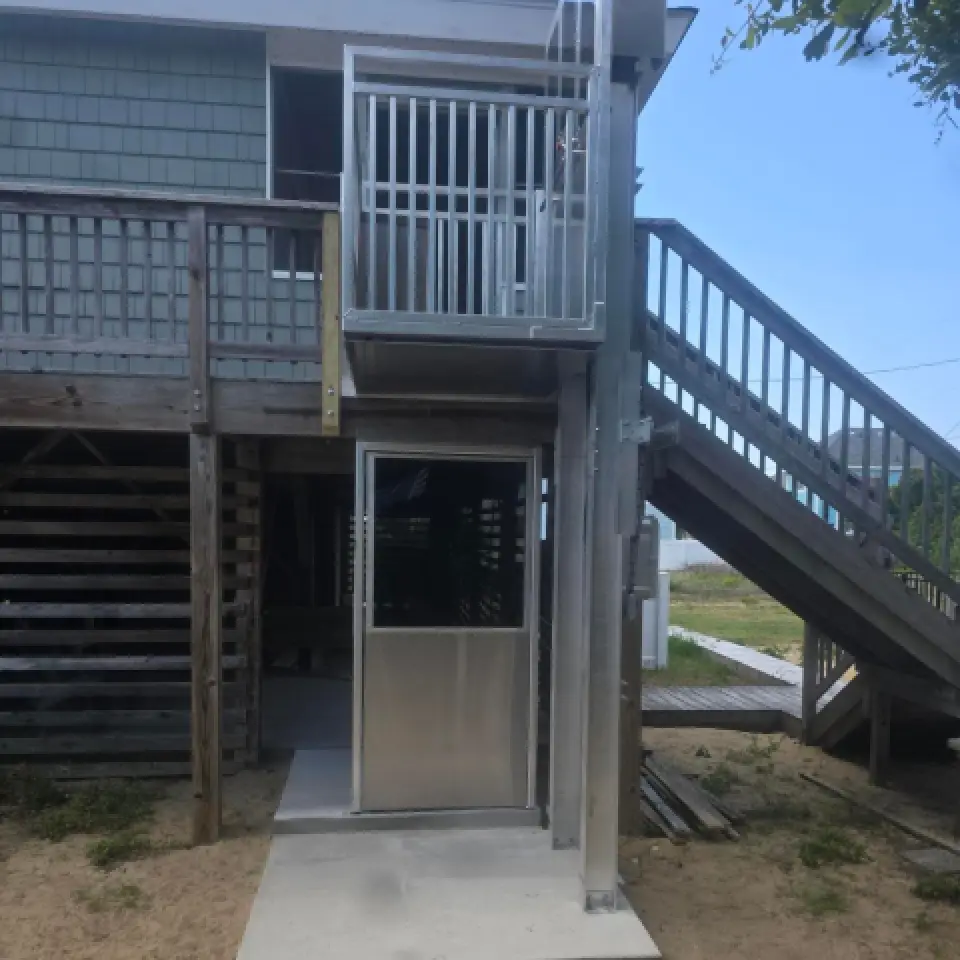 Outdoor wheelchair lift beside wooden stairs and deck attached to a raised house.