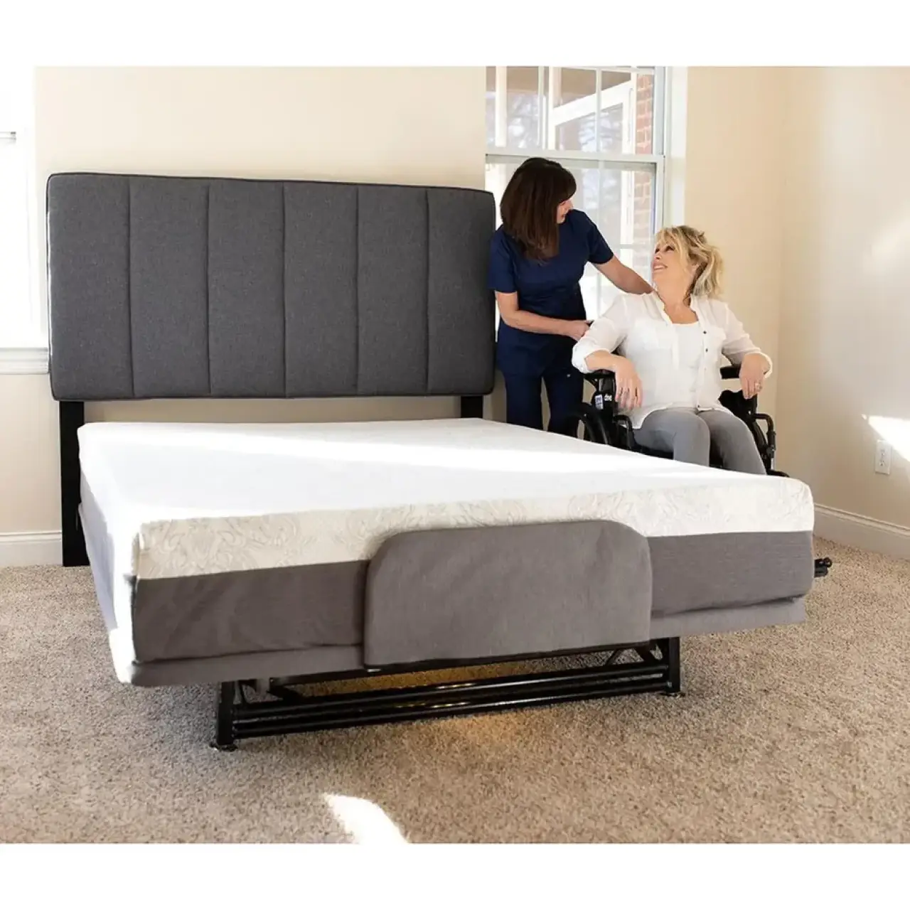 Caregiver assists a woman in a wheelchair beside an adjustable bed.