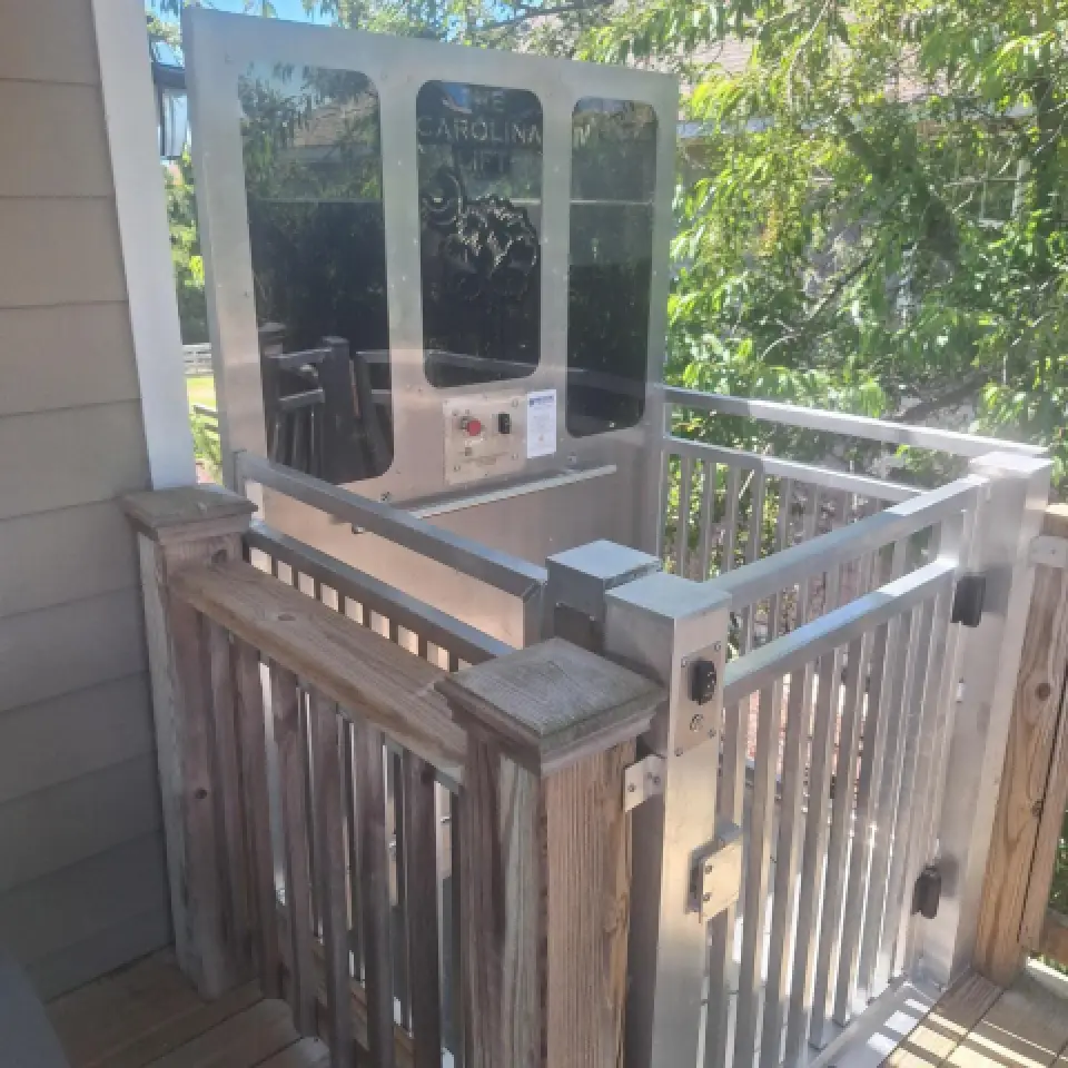 Outdoor residential platform lift elevator with metal railings and control panel, next to a porch.