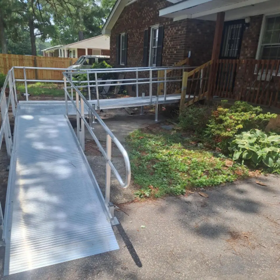 A metal wheelchair ramp leads from a driveway to a porch on a brick house.