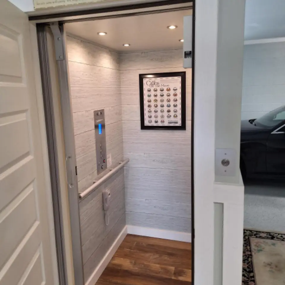 A home elevator with wood floors, control panel, and a framed chart on the wall.