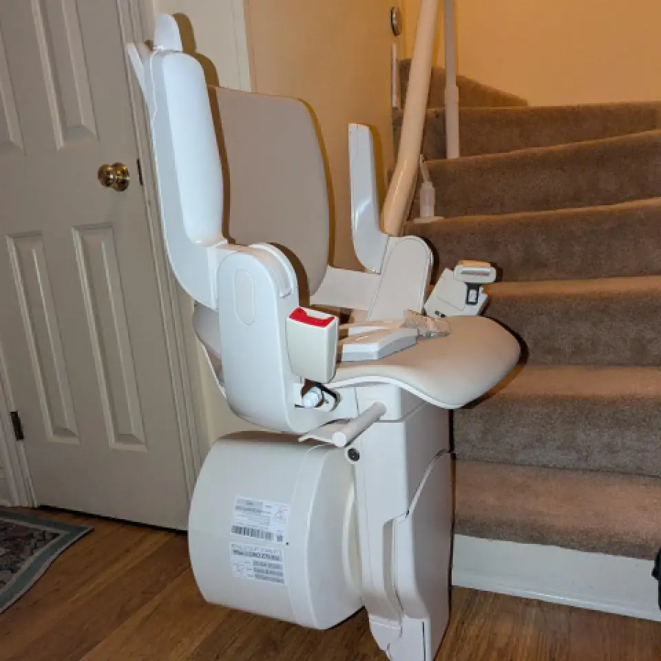 An Otolift stairlift chair is installed beside a carpeted curved staircase in a home.