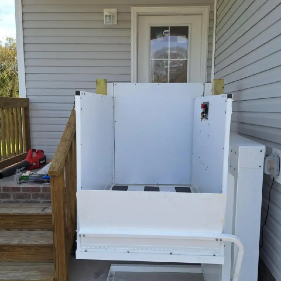 Outdoor wheelchair lift installed next to porch stairs leading up to a door of a house.