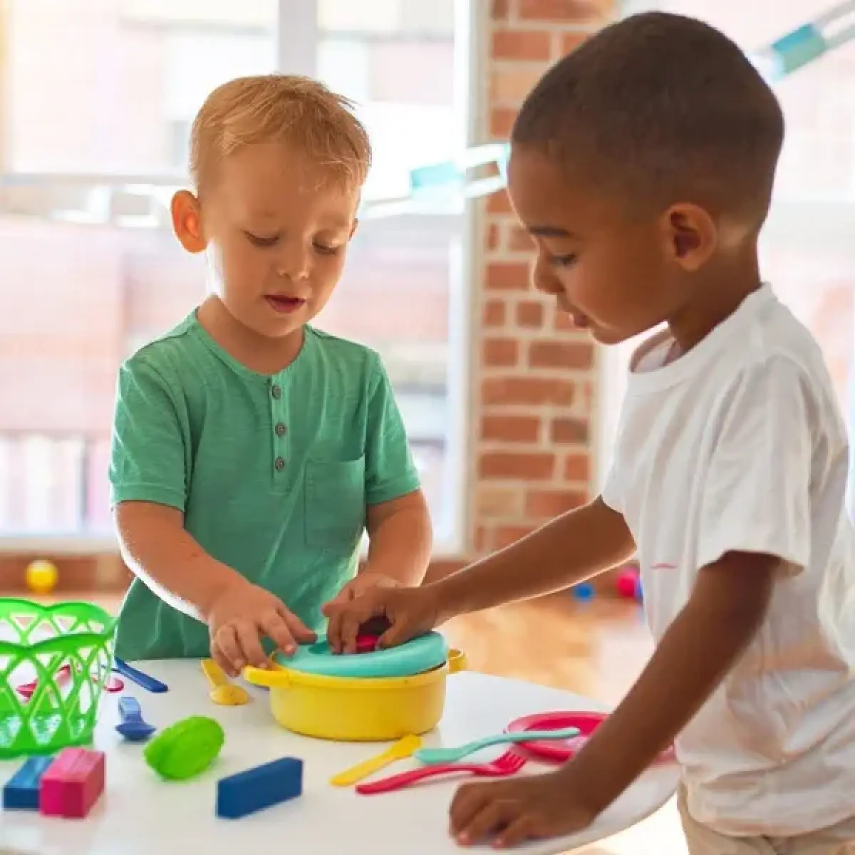 Two young children play with colorful modeling clay and tools at a table indoors.