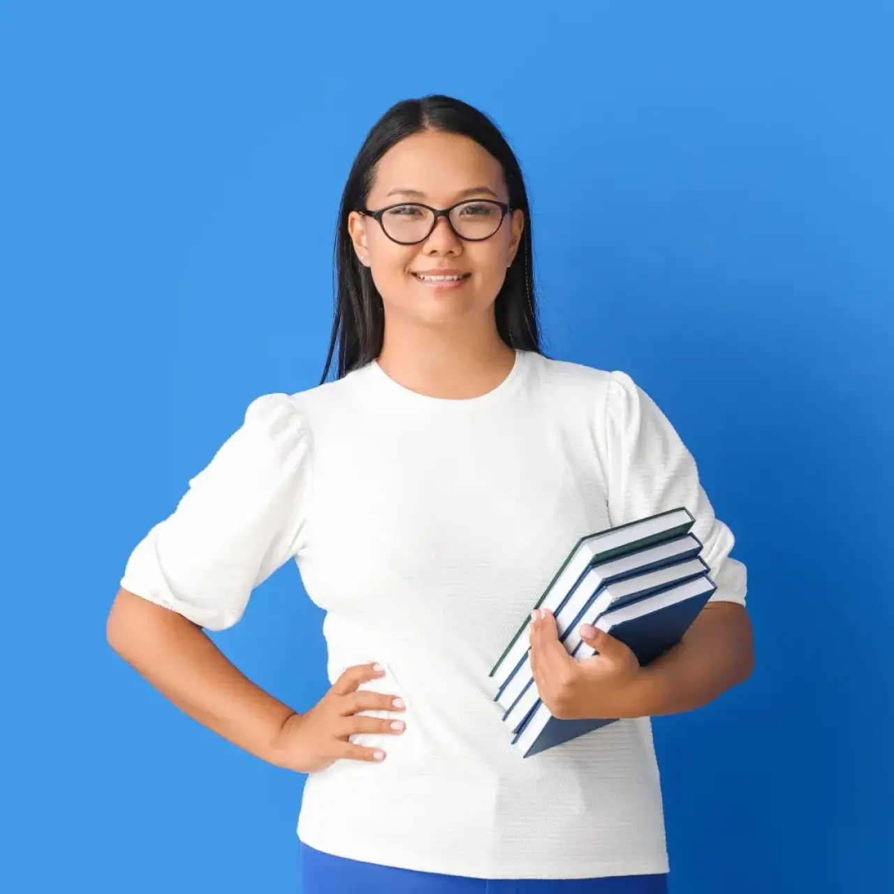 Smiling woman in glasses holding four books, standing against a solid blue background.
