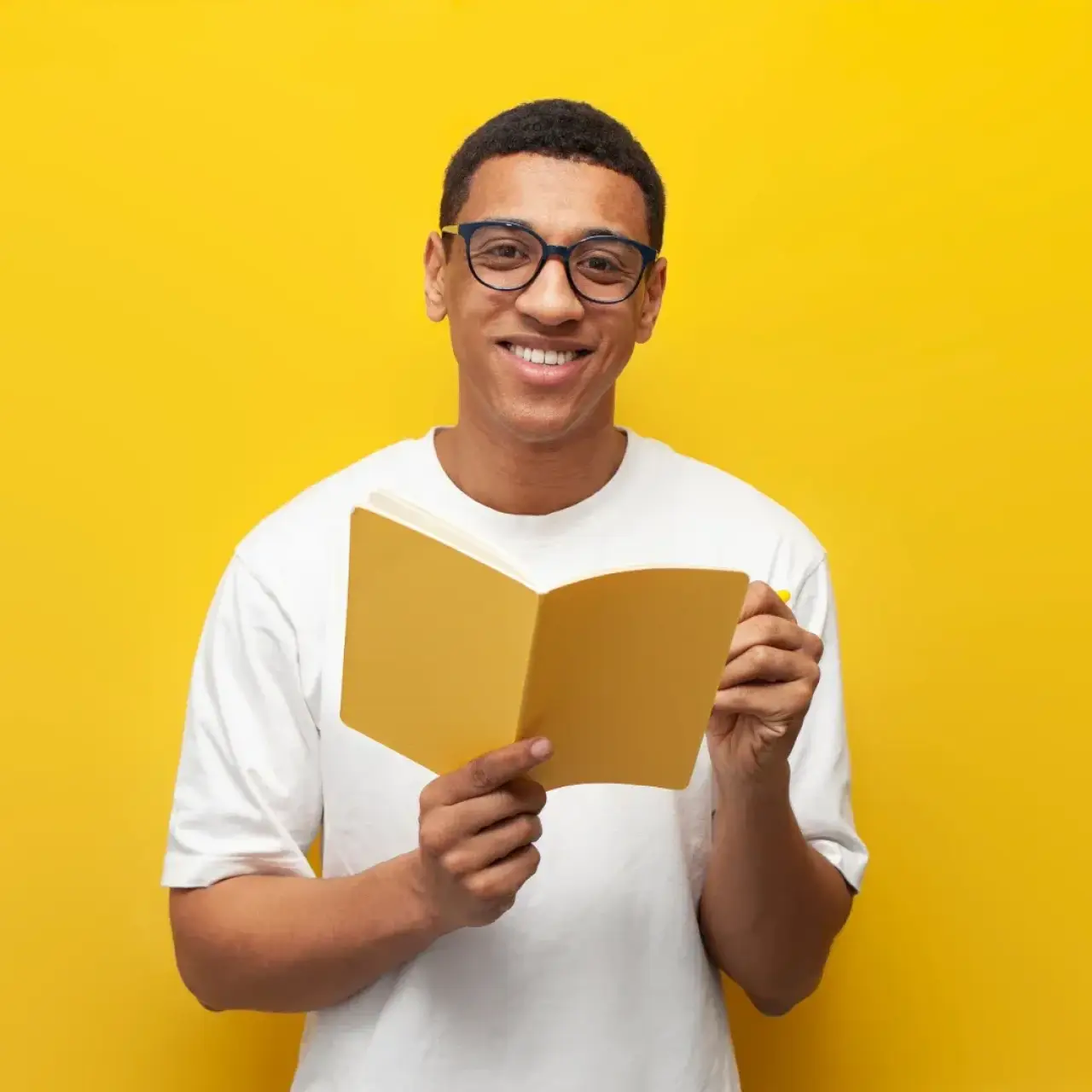 Smiling man in glasses holding a yellow book, standing against a bright yellow background.