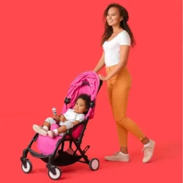 Woman smiles while pushing a baby in a pink stroller against a bright red background.
