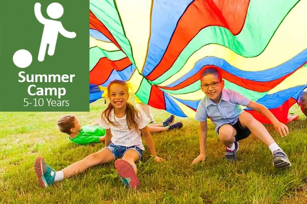 Three smiling kids play under a colorful parachute with a sign for Summer Camp ages 5–10.