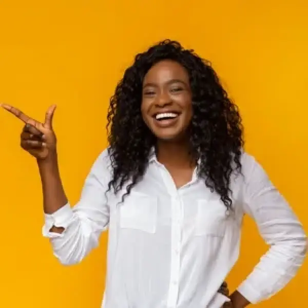 Smiling woman in a white shirt points sideways against a bright yellow background.