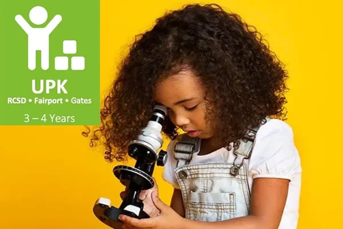 Young child with curly hair looks through a microscope against a bright yellow background.