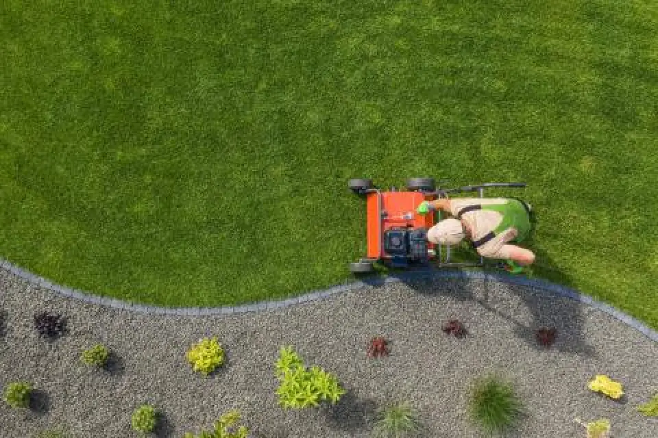 Person mowing lawn beside landscaped garden border