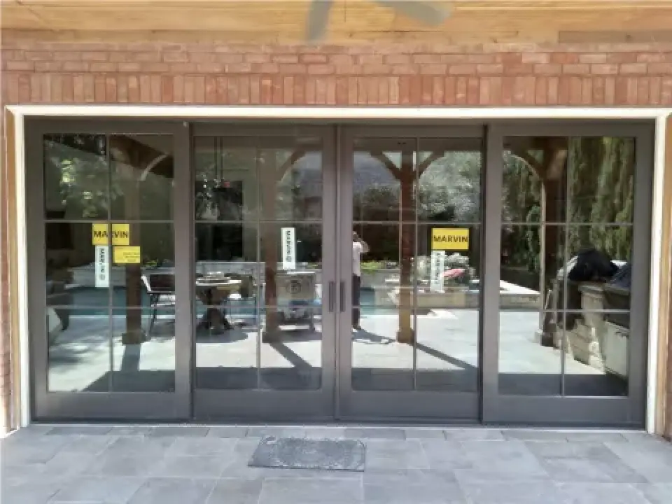 four glass patio doors with black frames, overlooking a backyard pool and outdoor furniture