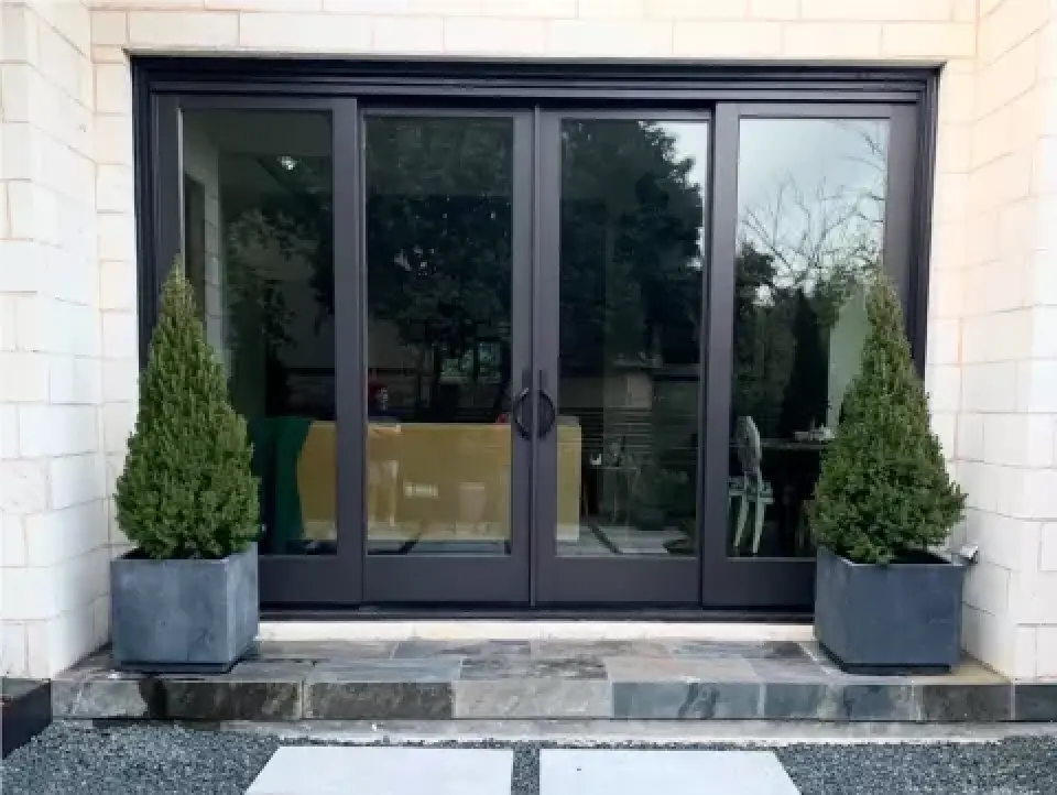 Sliding glass patio doors with black frames and evergreen planters