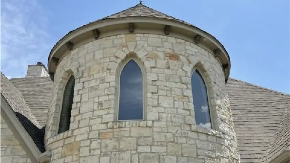 Round stone tower with two arched windows and a pointed roof under a blue sky.