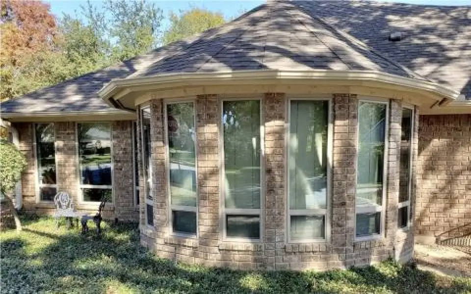 Curved brick house exterior with large bay windows and some greenery in front.