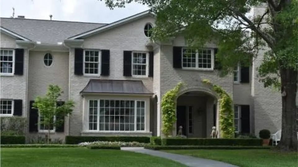 Two-story brick house with black shutters, large windows, and a well-kept front yard.
