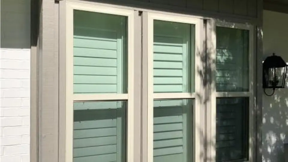 Double window with white trim and pale green shutters, next to an outdoor black wall lantern.