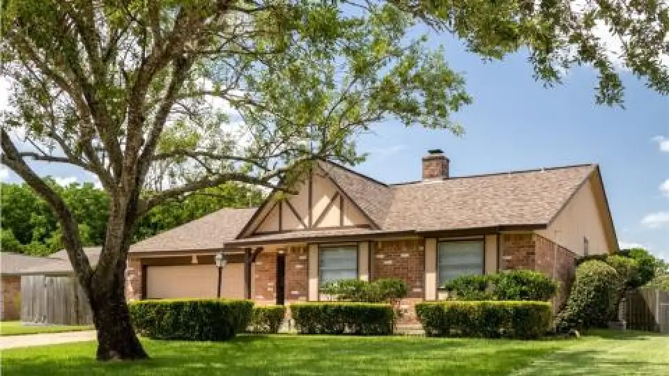 Single-story brick house with a gable roof, two-car garage, and trimmed shrubs in front yard.
