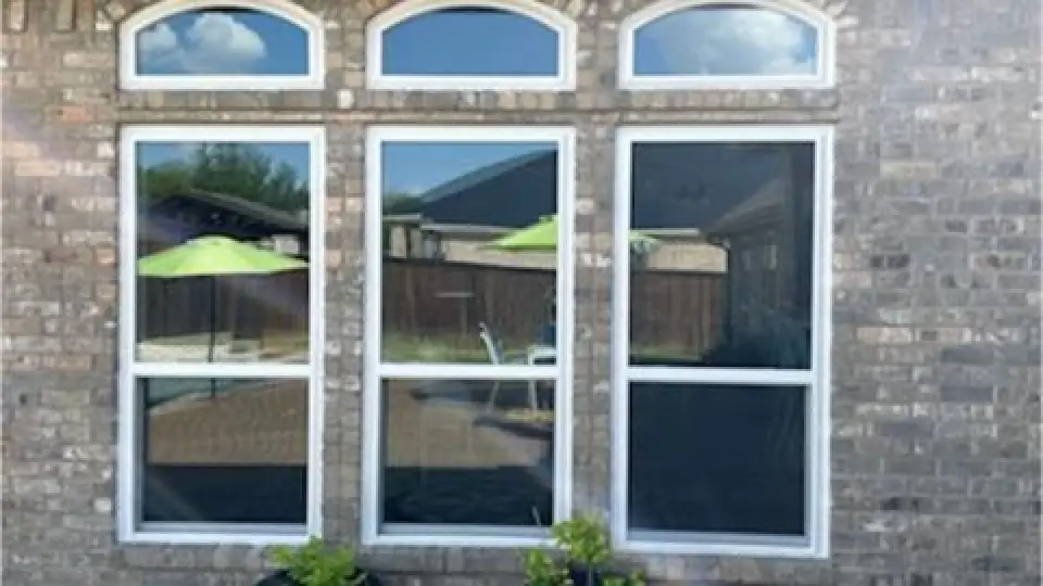 Three tall windows on a brick wall reflect a yard with green umbrellas and outdoor furniture.
