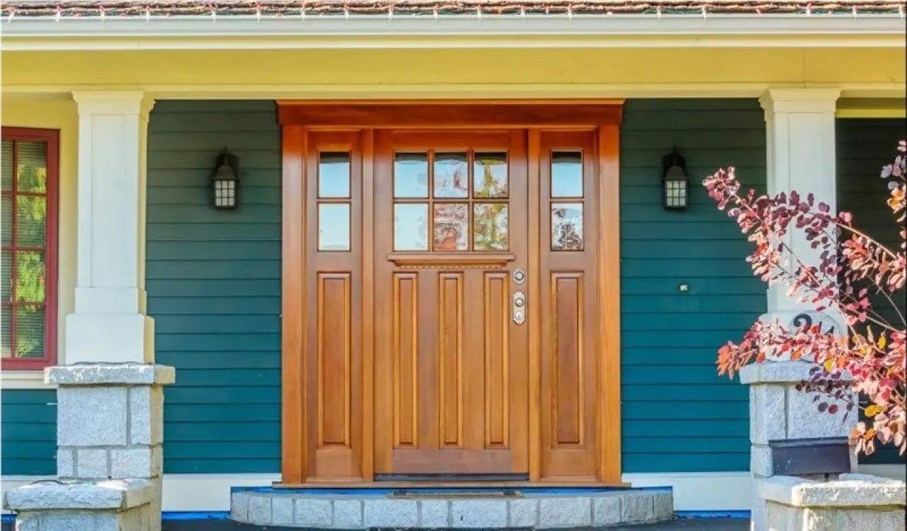 Wood entry door with sidelights on a covered front porch.