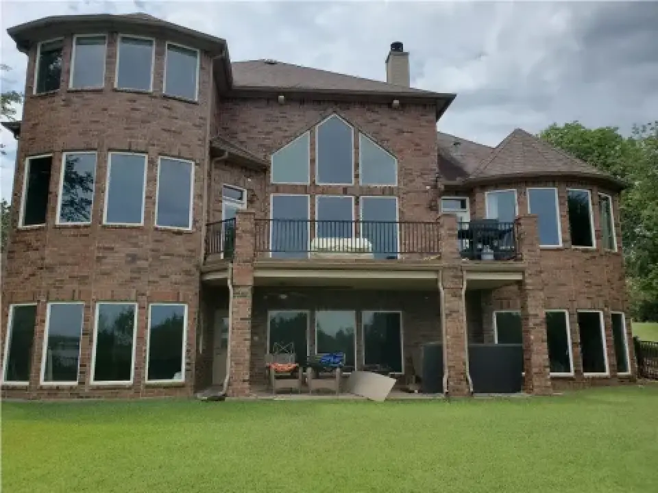 Large brick house with many windows, two stories, and a balcony, overlooking a grassy yard.