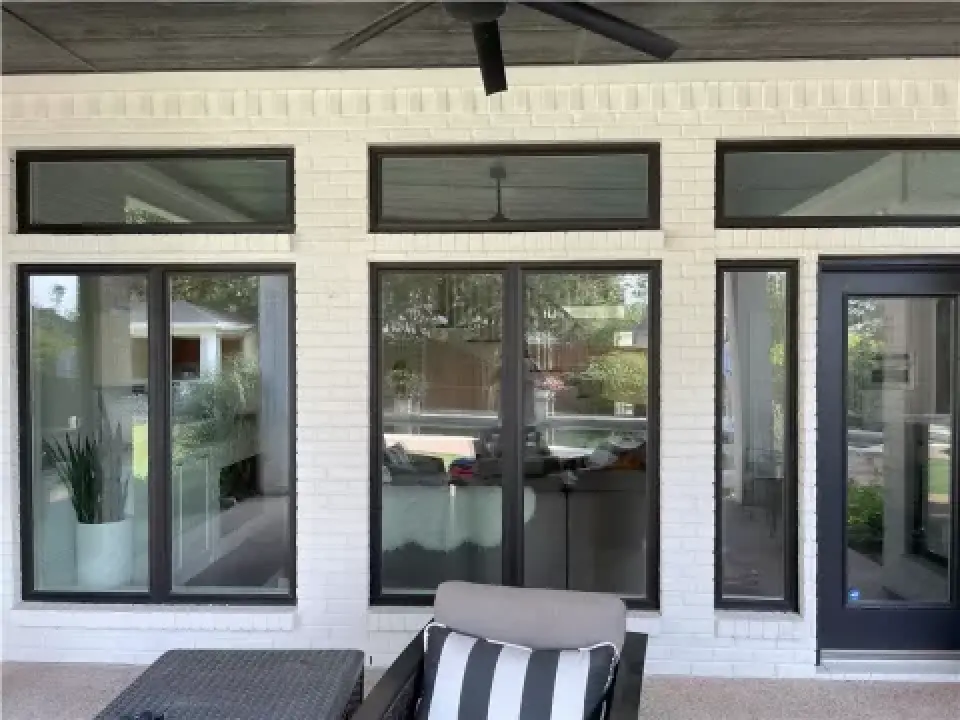 Large glass windows and doors with black frames on a white brick wall, viewed from a patio.