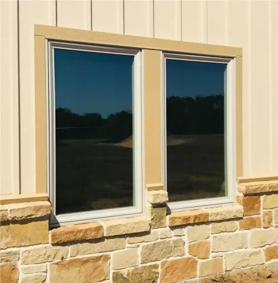 Two rectangular windows on a beige building with stone accents at the base, reflecting blue sky.