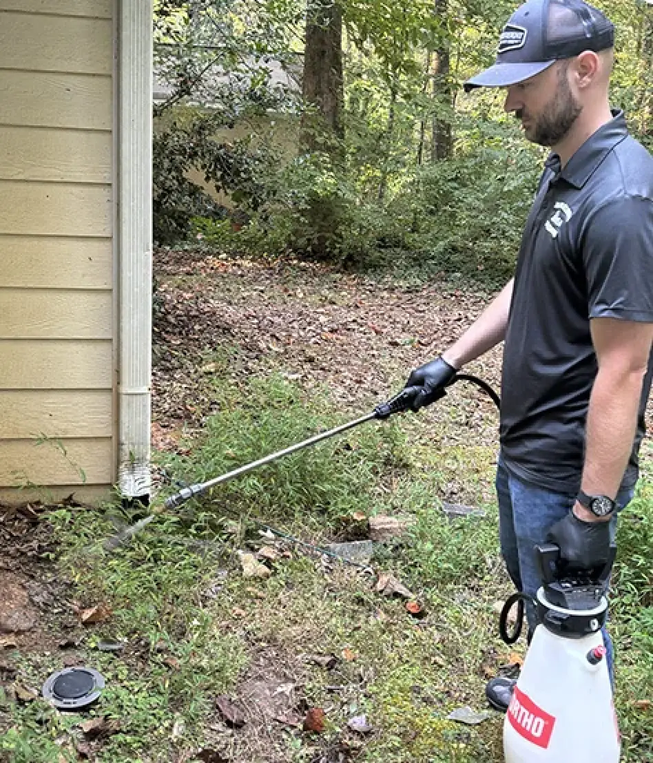 Pest control technician treating vegetation beside a North Georgia home.