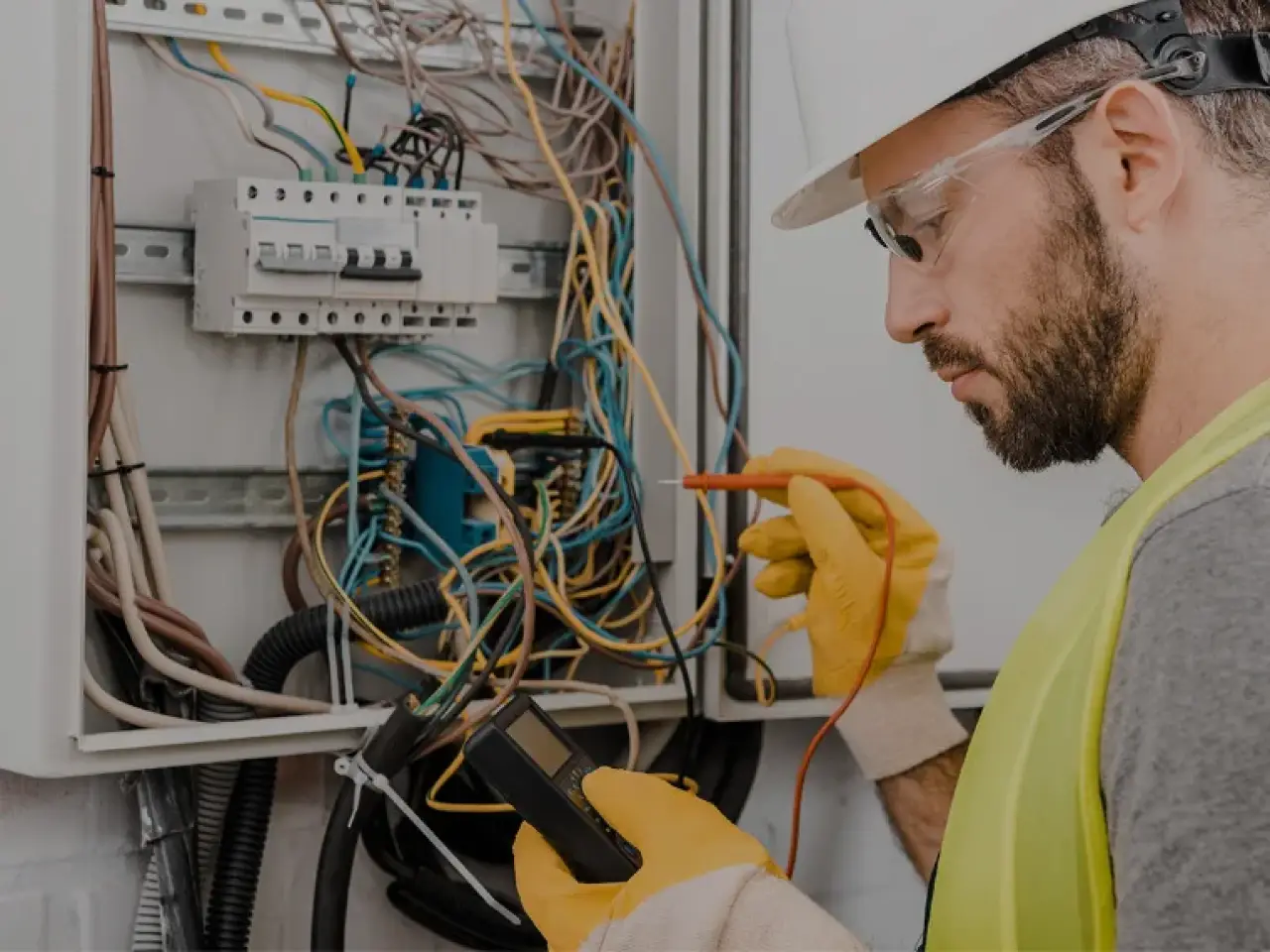 Electrician testing wiring inside an open electrical panel.
