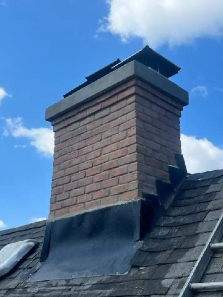 Brick chimney with black metal cap and flashing on a shingled roof.
