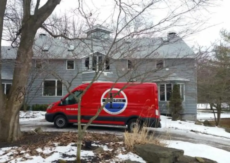 A red Empire Heating & Air Conditioning van in the driveway of a house with snow on the ground.